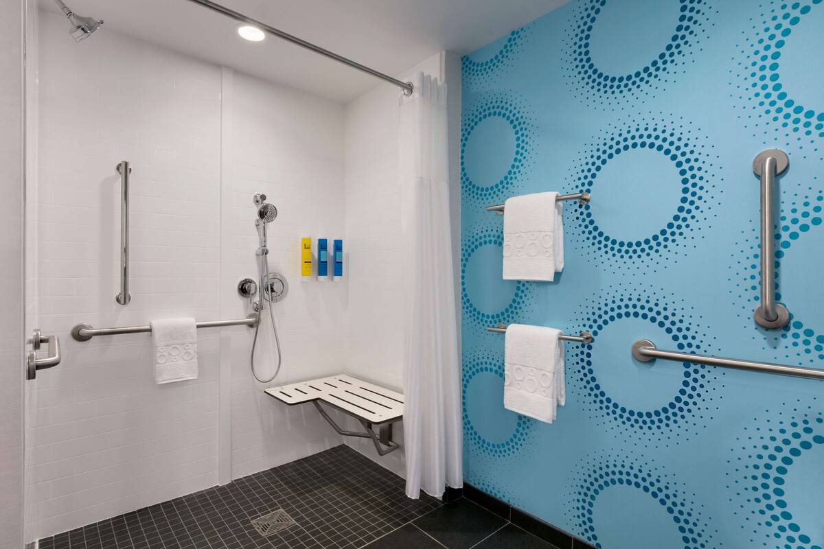 Un baño moderno con ducha, barras de apoyo, un banco y suelo de baldosas.