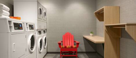 A laundry room with stacked towels, a red chair, and a wooden shelf.