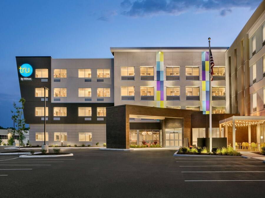 A hotel with a modern facade, multiple floors, and a parking lot in front.
