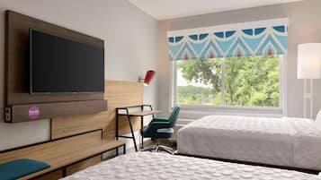 A hotel room with a bed, a desk, a chair, a TV, and a window with a view of trees.