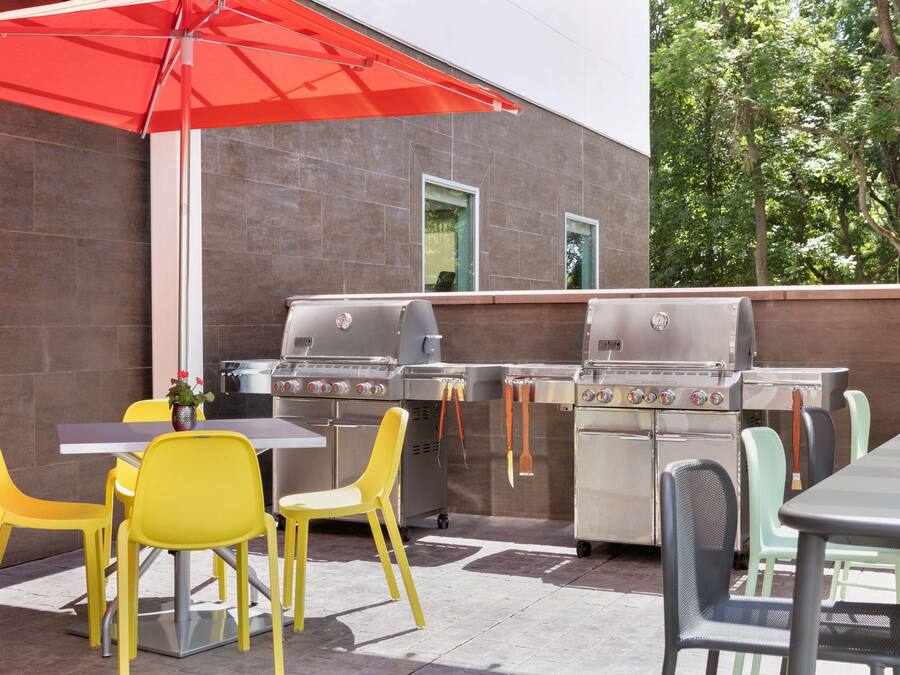 Un patio exterior con una parrilla, sillas amarillas y un paraguas rojo.