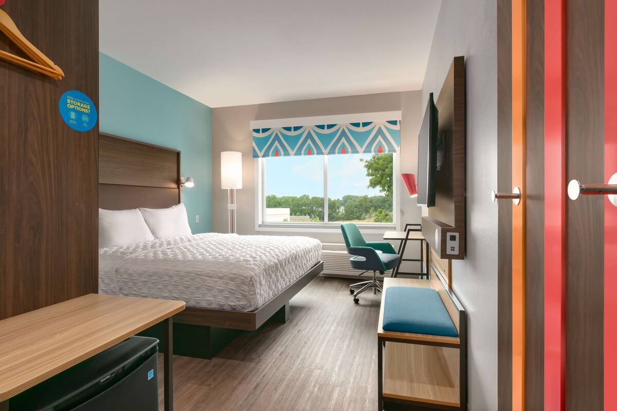 Habitación de hotel con cama, escritorio, silla, televisor y ventana con vistas.