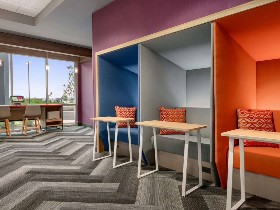 Een moderne lounge met zitplaatsen en tafels, grote ramen en een visgraat patroon in de vloerbedekking.