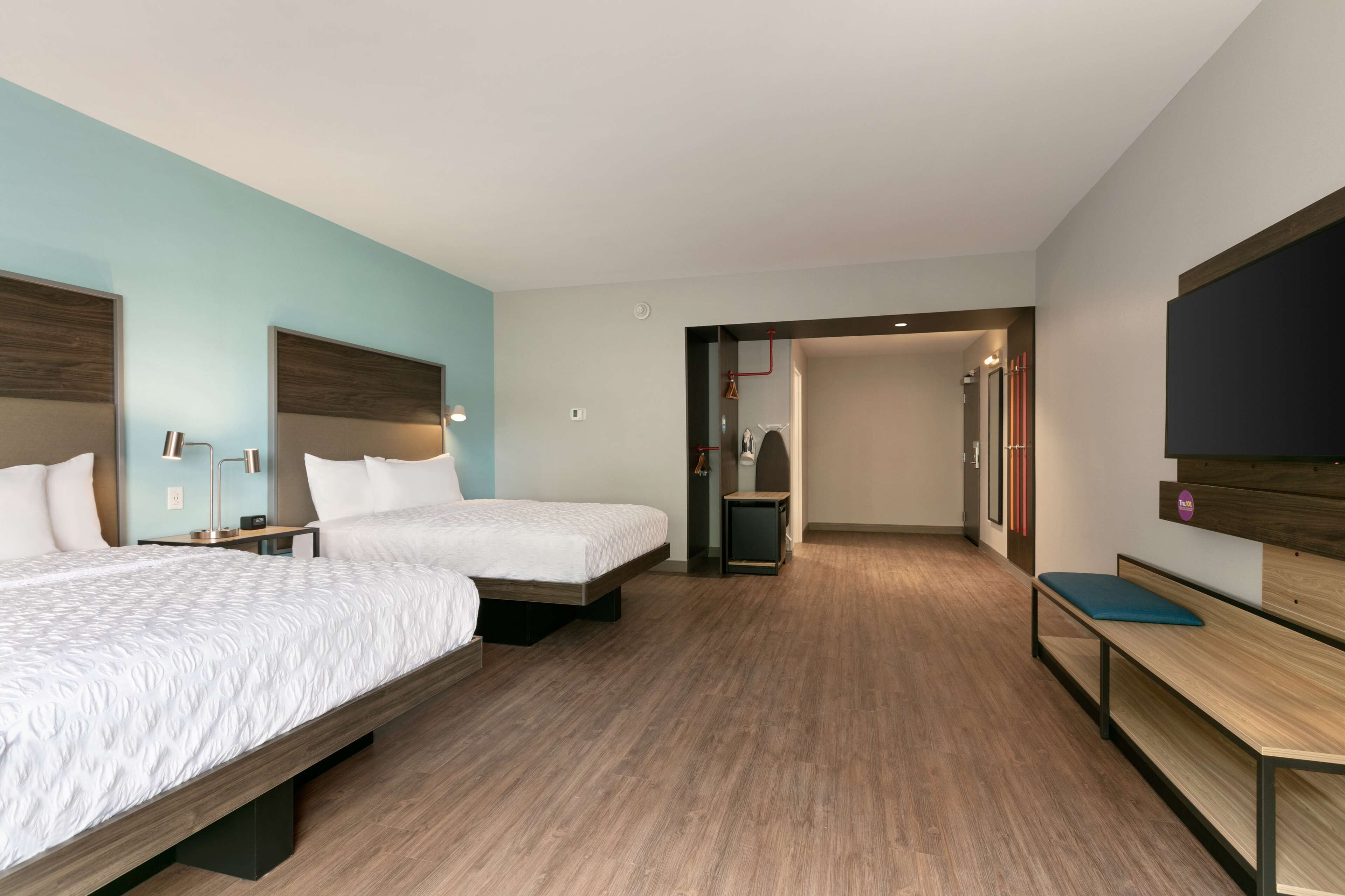 Une chambre d’hôtel avec deux lits, un banc en bois, une télévision et une petite table.