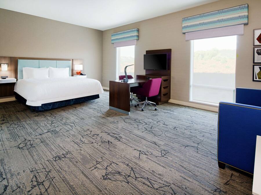 A hotel room with a large bed, a desk with a chair, a TV, and artwork on the walls.