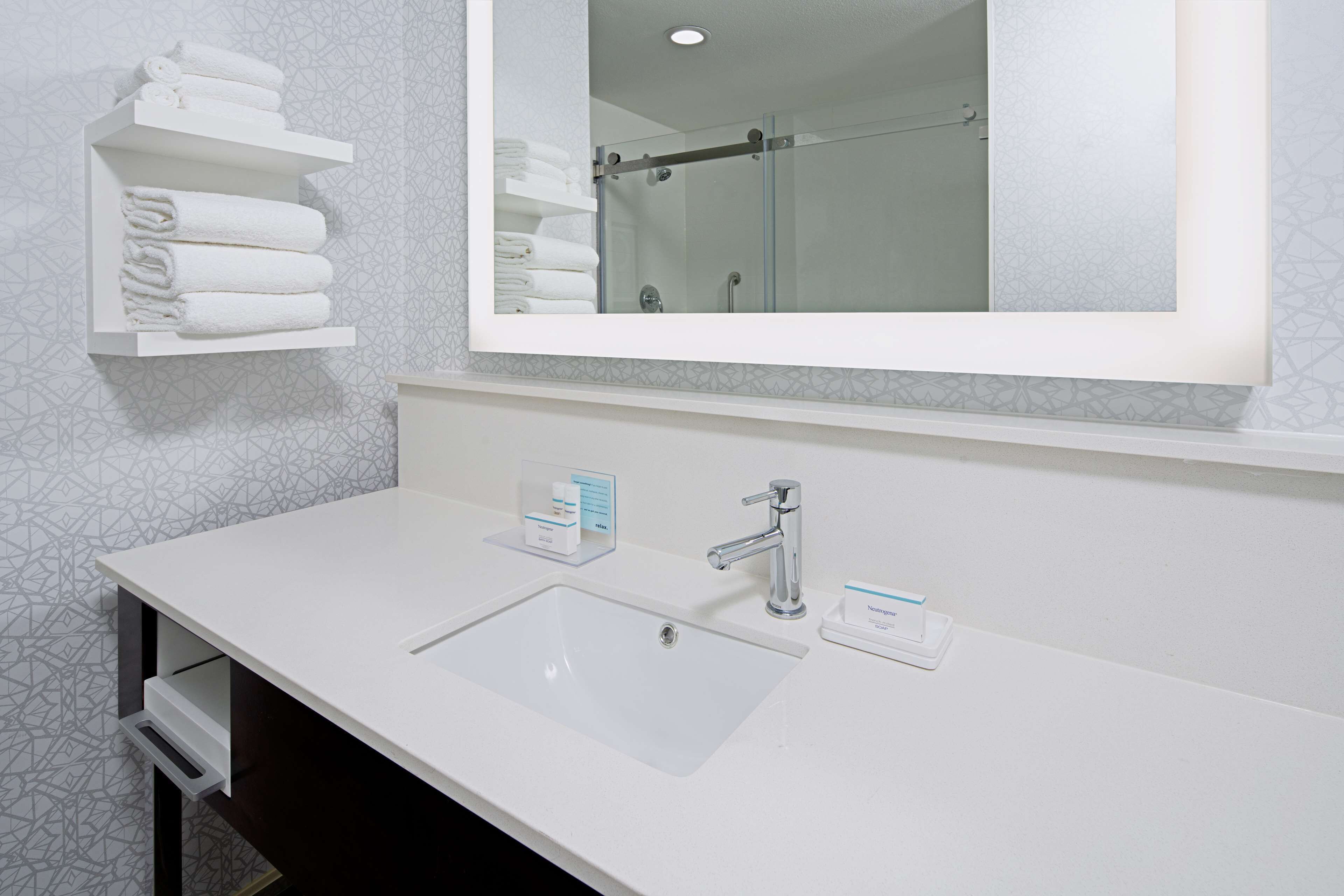 A bathroom with a white sink, a mirror, and a towel rack with folded towels.