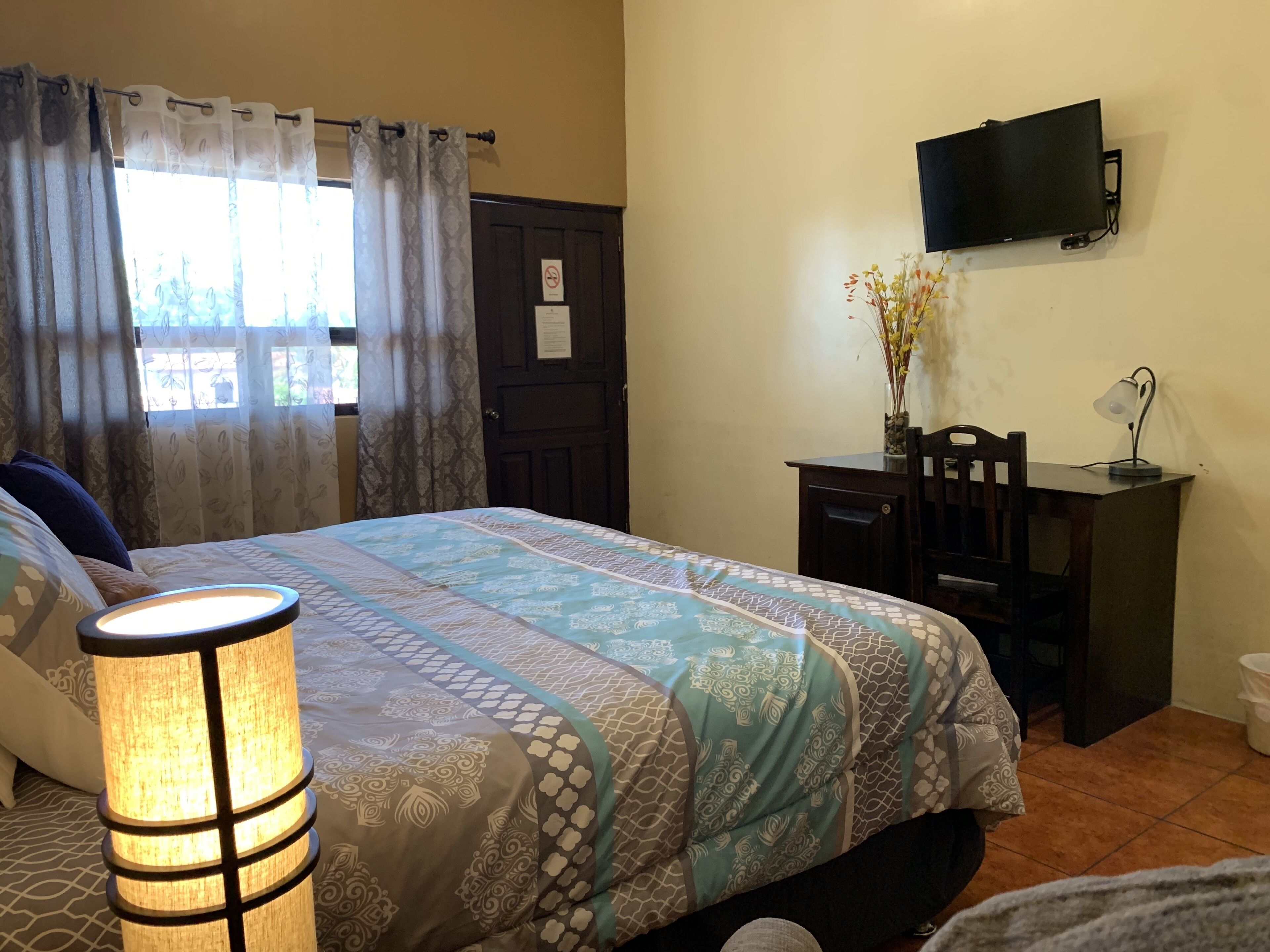 A bedroom with a bed, a desk, a chair, a TV, and a lamp.