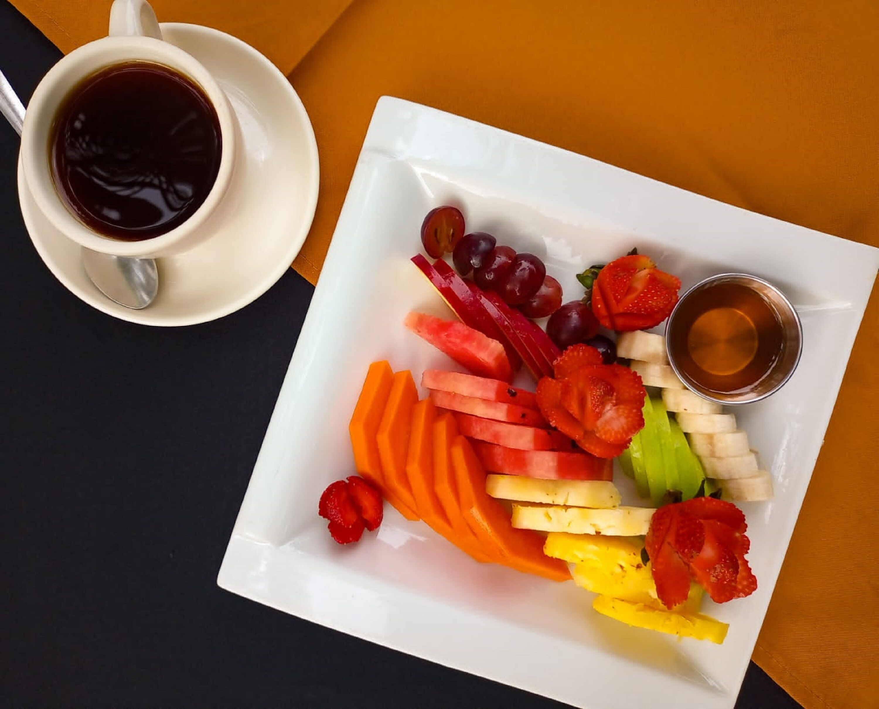 Una bandeja con frutas variadas y una taza de café sobre una mesa.