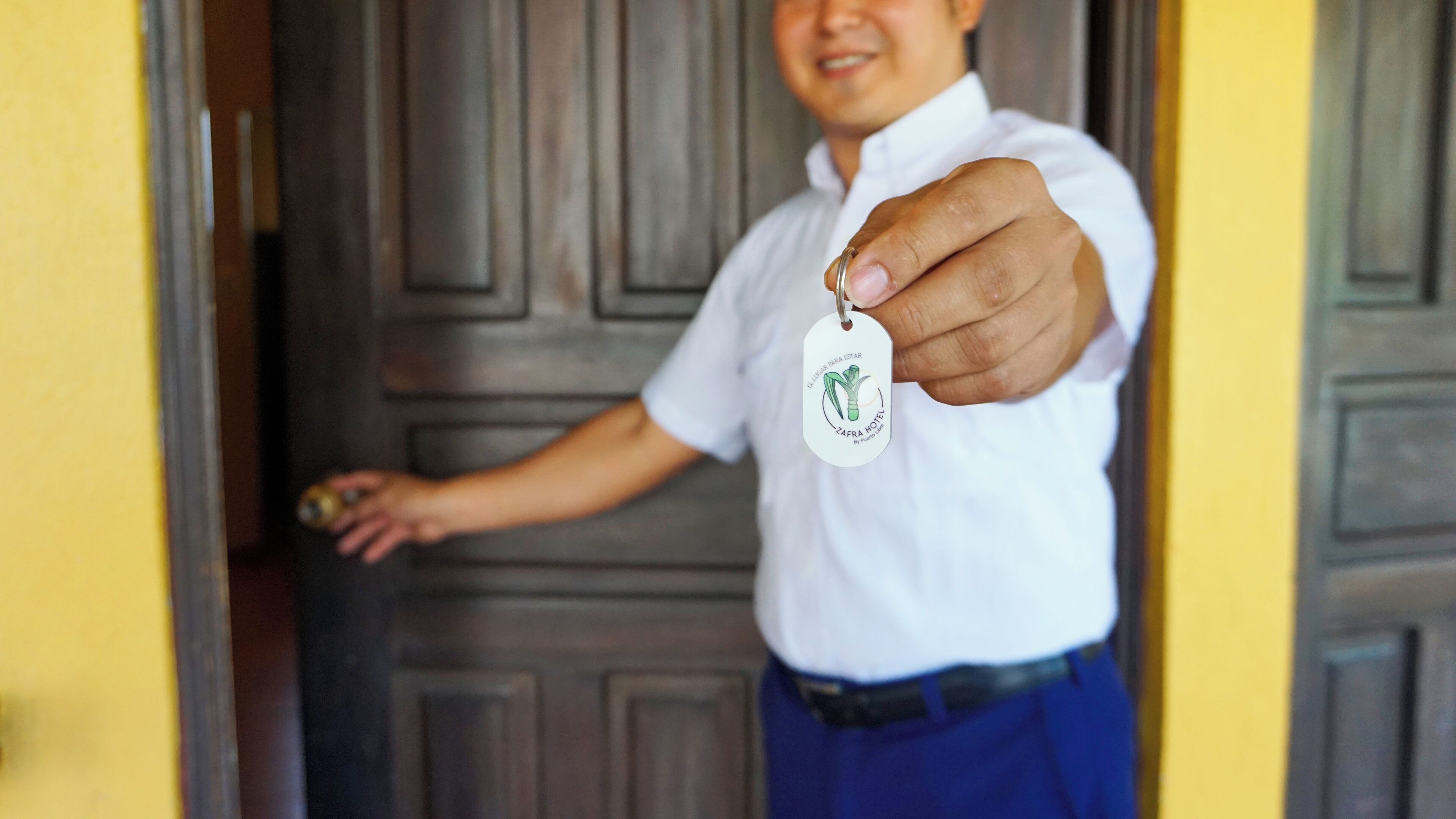 A person holding a keychain with a hotel logo, standing in front of a wooden door.