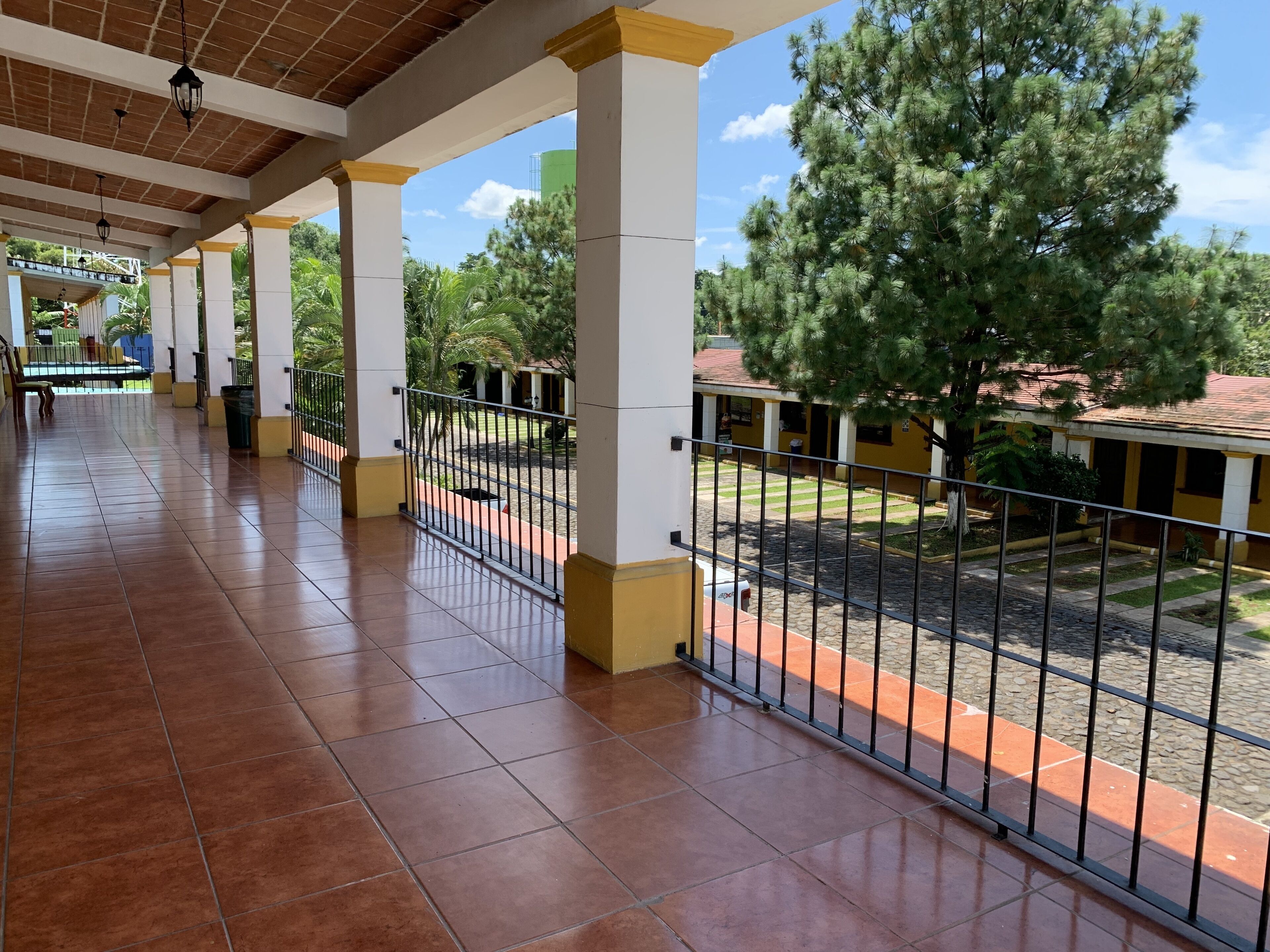 A covered outdoor area with tiled flooring, metal railings, and a view of a building with a tiled roof.