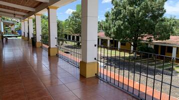A covered outdoor area with tiled flooring, metal railings, and a view of a building with a tiled roof.