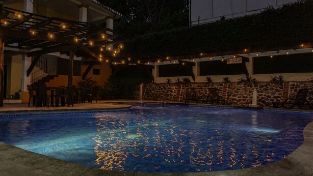 A swimming pool with a stone wall and string lights. - Zafra Hotel (San Martín Zapotitlán)