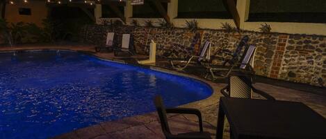 An outdoor swimming pool with lounge chairs and a stone wall.