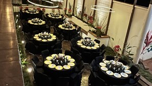 An outdoor dining area with multiple round tables, each set with black chairs and yellow tablecloths. The area is illuminated by string lights and has potted plants and flowers around the tables. - Zafra Hotel (San Martín Zapotitlán)