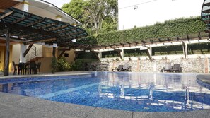 A swimming pool with a tiled deck, outdoor seating, and a covered area with stairs. - Zafra Hotel (San Martín Zapotitlán)