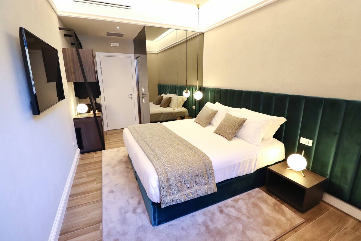 A modern bedroom with a bed, bedside tables, a mirror, and a nightstand with a lamp.