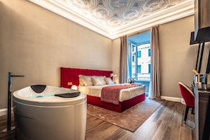 Ett modernt hotellrum med en röd säng, ett badkar och utsikt över en byggnad genom ett fönster.