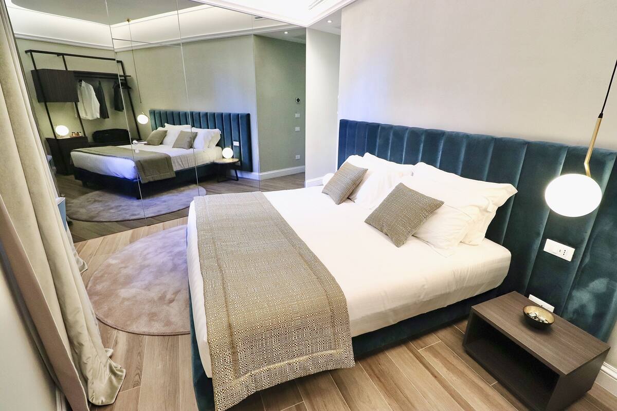 A modern hotel room with a large bed, a smaller bed, a nightstand, and a mirror.