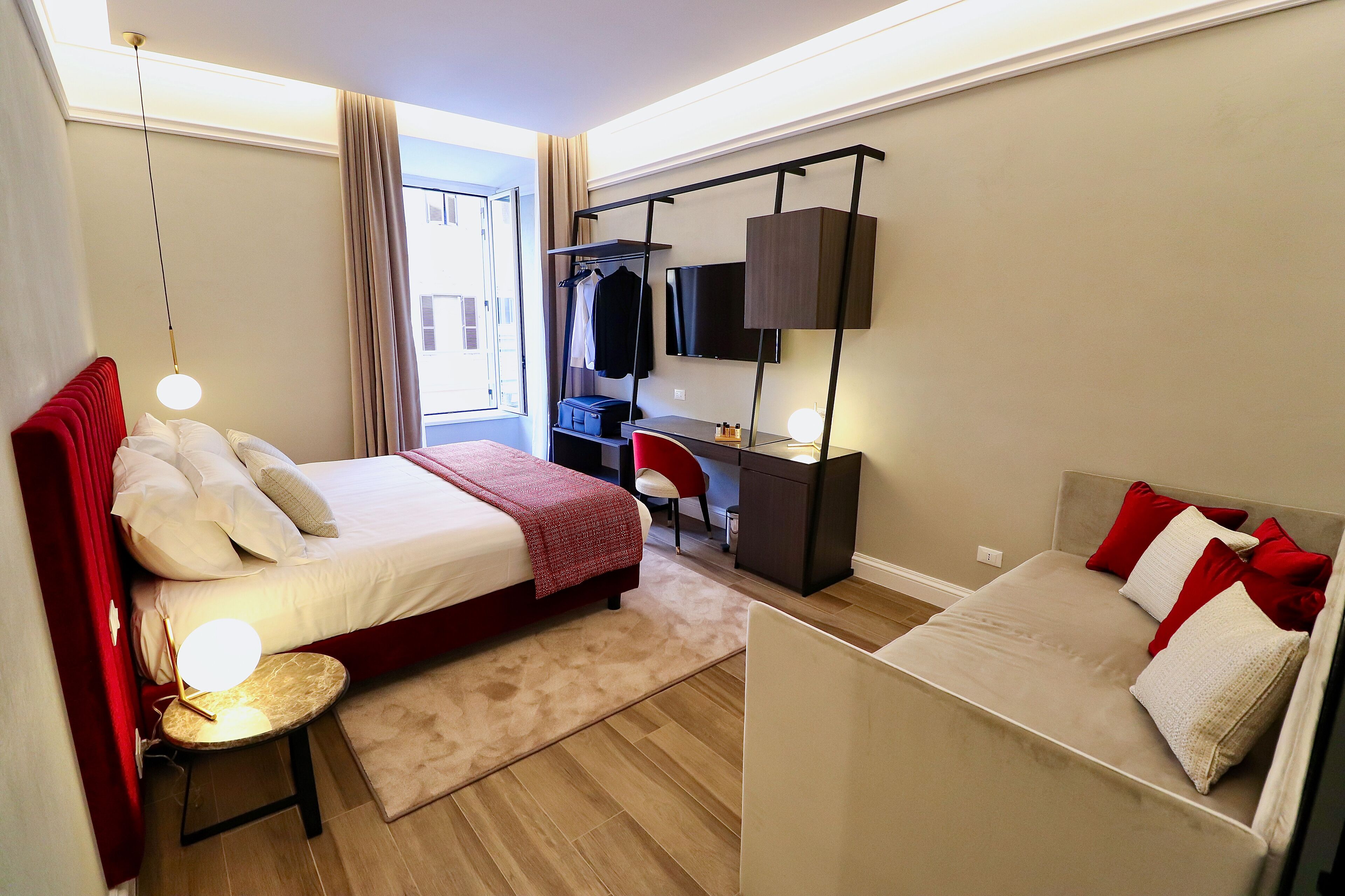 A modern hotel room with a large bed, a desk with a computer, a TV, and a wardrobe.