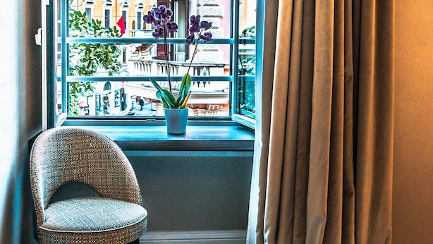 A balcony with a chair, a potted plant, and a view of buildings. - Growel Exclusive Suites San Pietro (Rome)