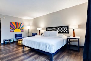 Una habitación de hotel con una cama, dos mesitas de noche, una obra de arte en la pared, una silla y una pequeña mesa redonda.