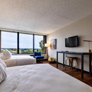 A hotel room with two beds, a desk, a chair, a TV, and a view of the outdoors. - The Bohemian (Iowa City)