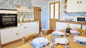 A kitchen with white cabinets, a wooden table set for dining, and a microwave. - This well-equipped cottage is perfect for a family or group holiday. (Hinderwell, near Whitby)