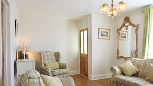 A living room with a plaid sofa set, a matching armchair, a wooden coffee table, and a chandelier. - This well-equipped cottage is perfect for a family or group holiday. (Hinderwell, near Whitby)