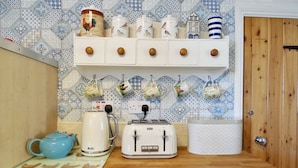A kitchen with a wooden countertop, a white toaster, a kettle, and a blue teapot. Above the counter, there are shelves with various kitchen items and a wall with patterned tiles. - This well-equipped cottage is perfect for a family or group holiday. (Hinderwell, near Whitby)