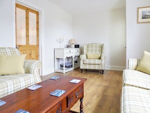 Un salon avec une table basse en bois, deux canapés à carreaux, un fauteuil à carreaux et une table d’appoint blanche avec une lampe.