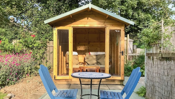 A wooden cabin with a sliding glass door, two blue chairs, and a small round table. - This well-equipped cottage is perfect for a family or group holiday. (Hinderwell, near Whitby)