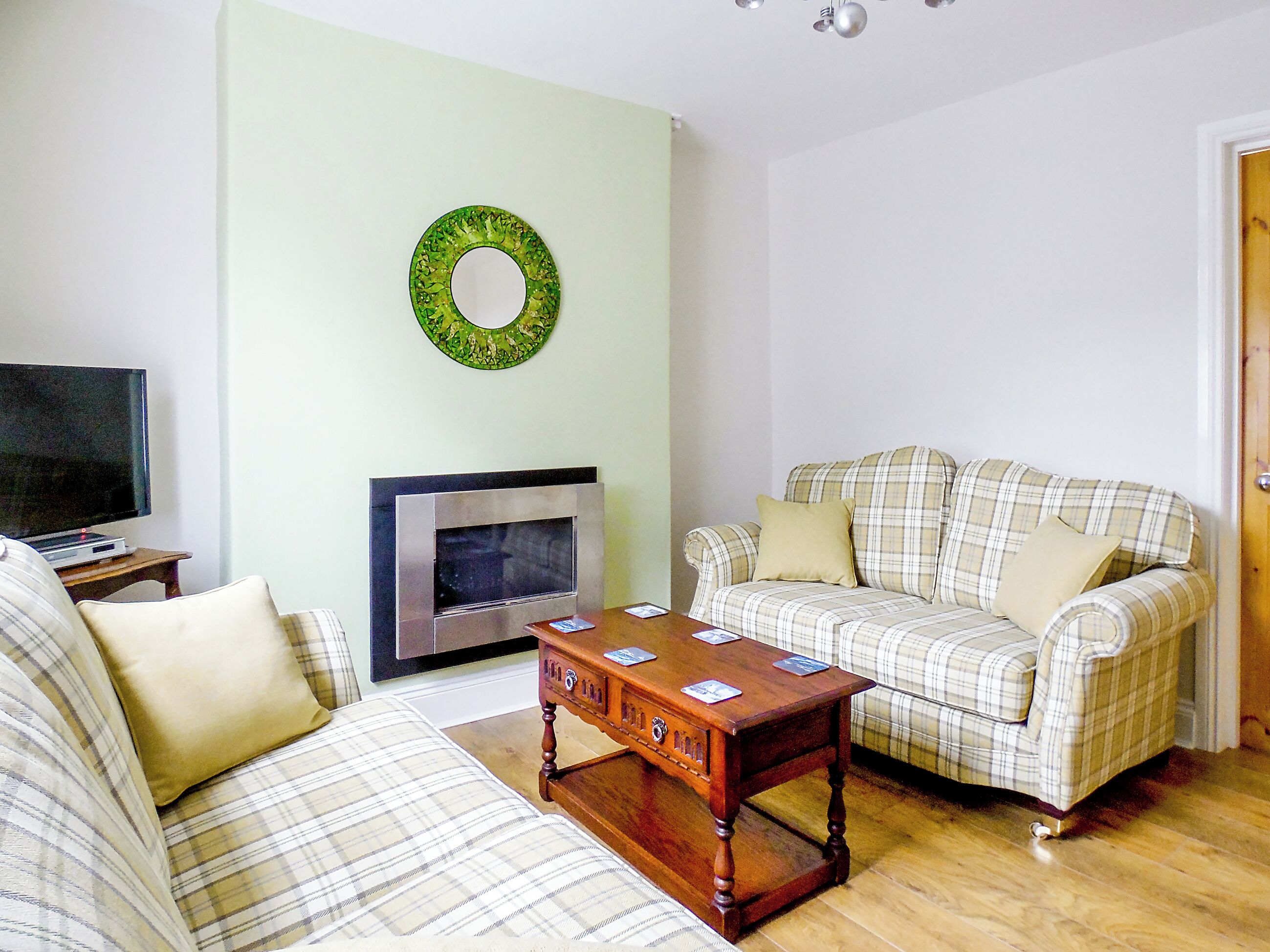 A living room with a sofa, a coffee table, a flat-screen TV, a fireplace, and a green wreath on the wall.