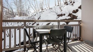 Un balcone con tavolo e due sedie, affacciato su un paesaggio innevato con alberi e una collina.