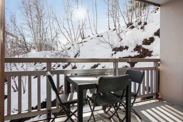 Un balcon avec une table et deux chaises, donnant sur un paysage enneigé avec des arbres et une colline.