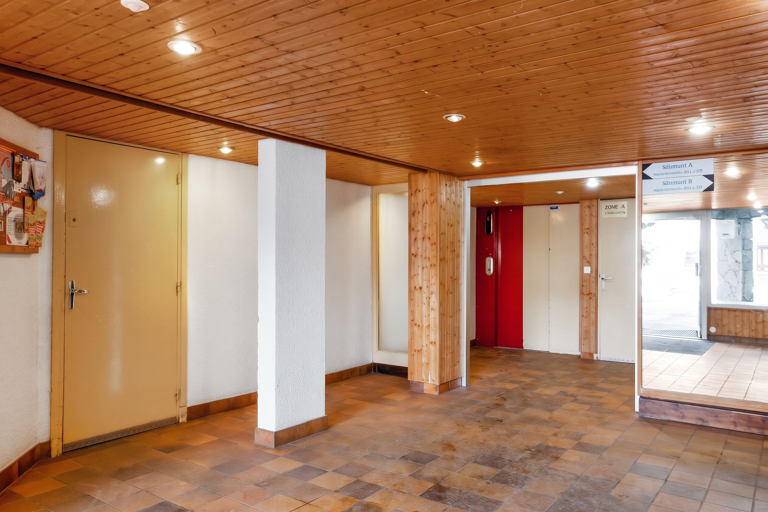 A hallway with wooden ceiling and tiled flooring, leading to doors labeled 'Sämtum A' and 'Sämtum B'.
