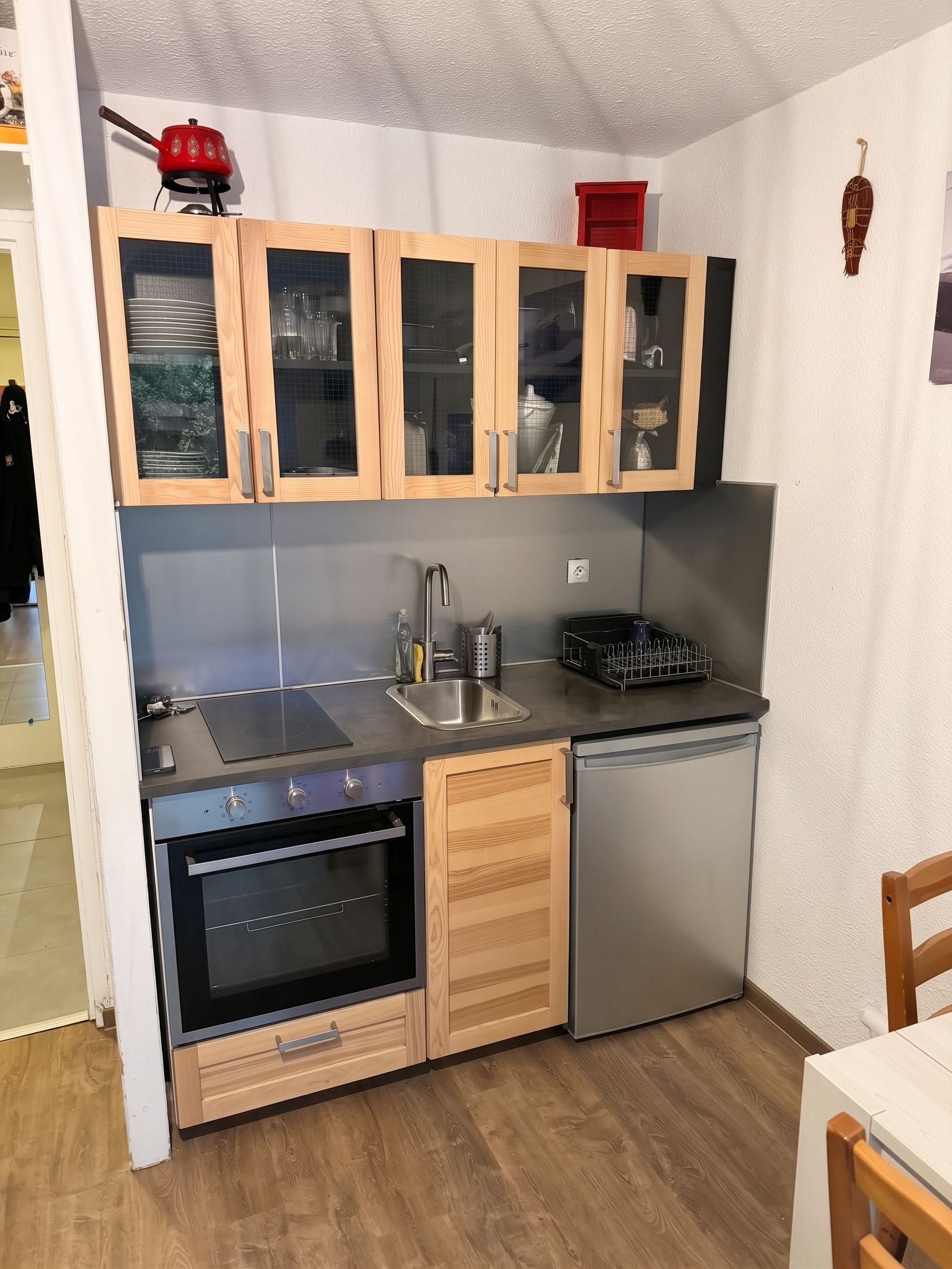 Een compacte keuken met een fornuis, oven en koelkast, houten kastjes en een klein spoelbakje.