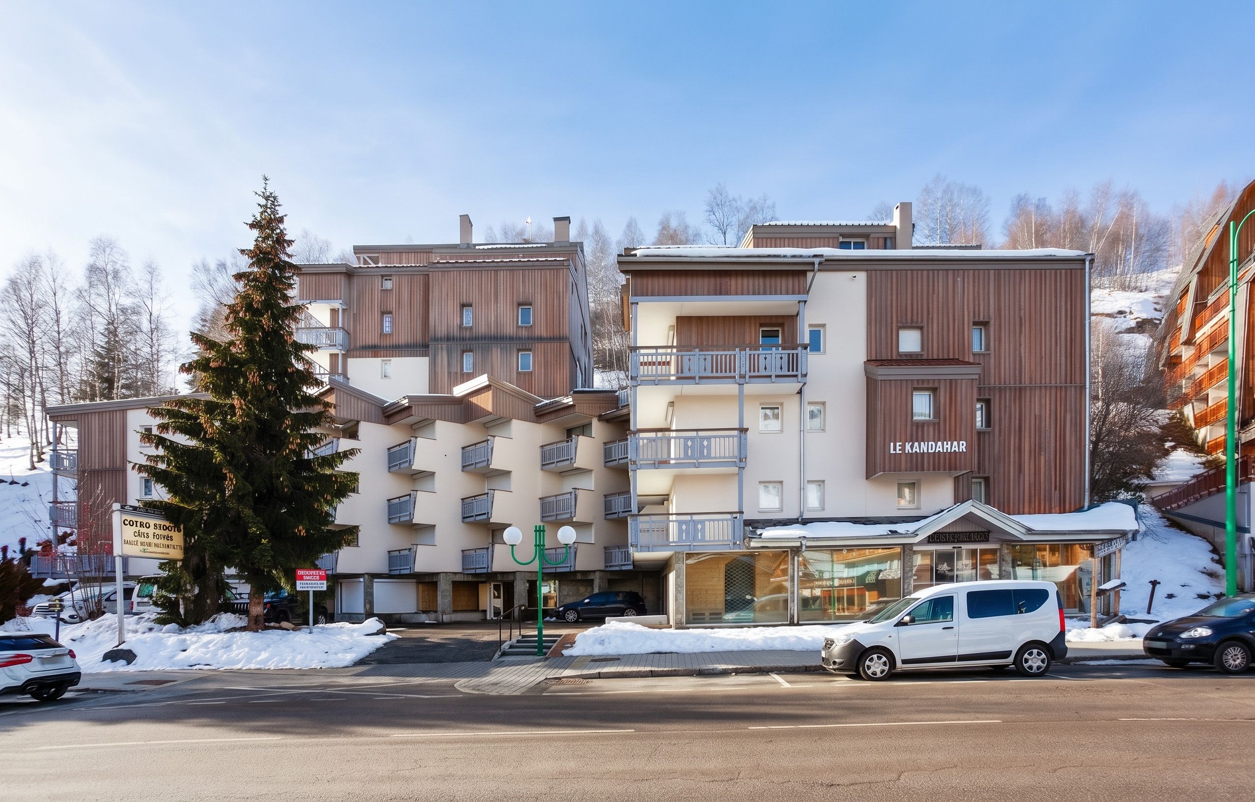 A multi-story hotel with balconies, a parking area, and a snow-covered landscape.