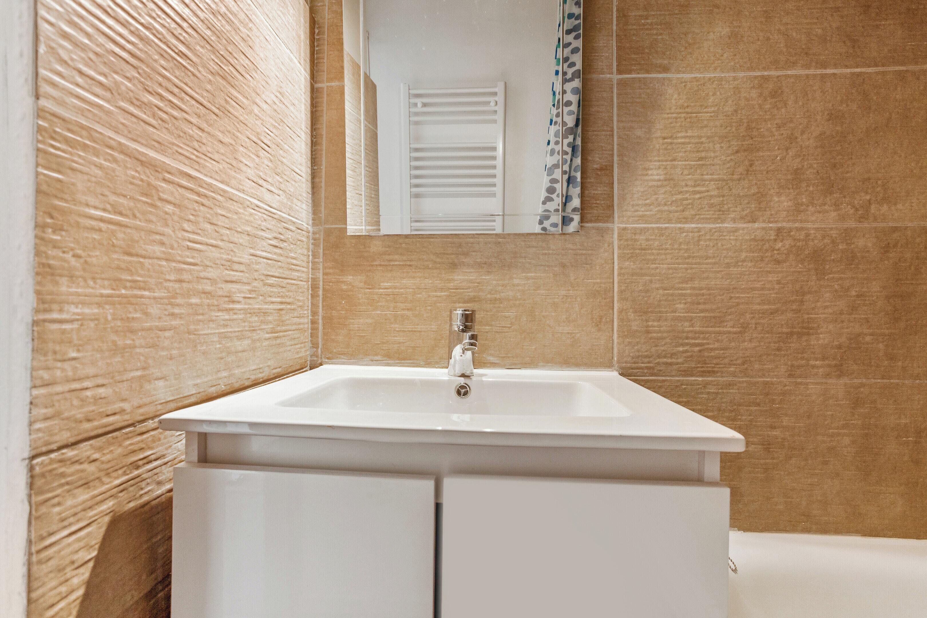 Un baño con lavamanos blanco, un espejo y cortina de ducha.