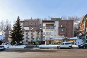 Un hôtel à plusieurs étages doté de balcons, un panneau indiquant la présence d’une station de ski, et un espace de stationnement enneigé.