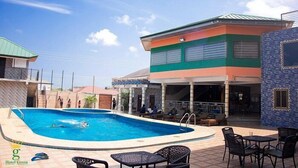 A swimming pool area with lounge chairs and a covered seating area. - Hotel Green (Accra)