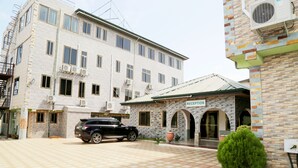 A building with a reception area, a black SUV parked in front, and a paved driveway. - Hotel Green (Accra)