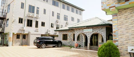 A building with a reception area, a black SUV parked in front, and a paved driveway.