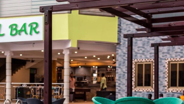 An outdoor seating area with green chairs and a pool. - Hotel Green (Accra)