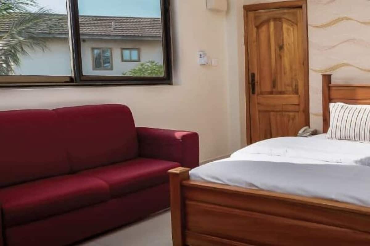 A bedroom with a wooden bed, a red sofa, a wooden door, and a patterned wall.
