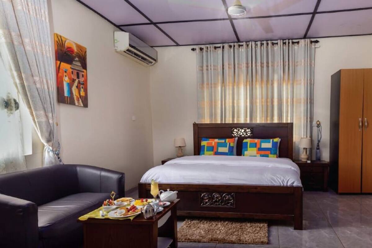 A bedroom with a bed, a chair, a table with breakfast items, a wardrobe, and a painting on the wall.