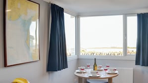 A room with a dining table set for four, a fruit bowl, a map on the wall, and a view of the sea through large windows. - 2 bedroom accommodation in Southerness, near Dumfries (Southerness, near Dumfries)