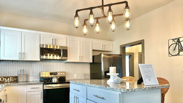 A modern kitchen with white cabinets, a built-in oven, a microwave, and a stainless steel refrigerator. - Southern Staycation! (Greenville)