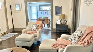 A living room with a sofa, armchairs, a coffee table, and a lamp. There is a door leading to another room and a window with blinds. - Southern Staycation! (Greenville)