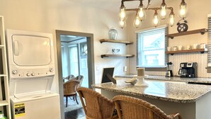 A kitchen with a built-in washer, wicker bar stools, a granite countertop, and a hanging light fixture. - Southern Staycation! (Greenville)