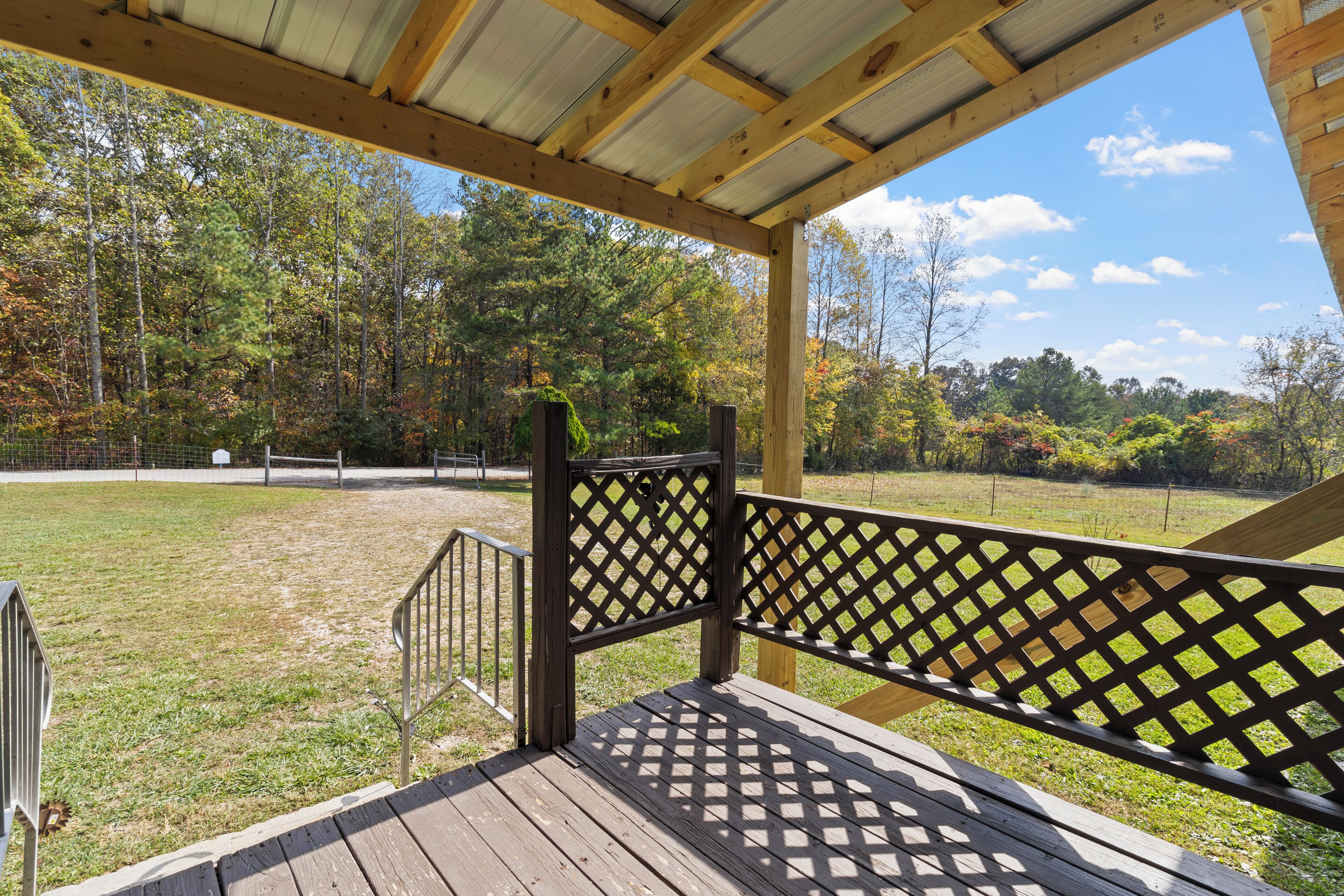 A wooden deck with a lattice railing overlooking a fenced field and trees.